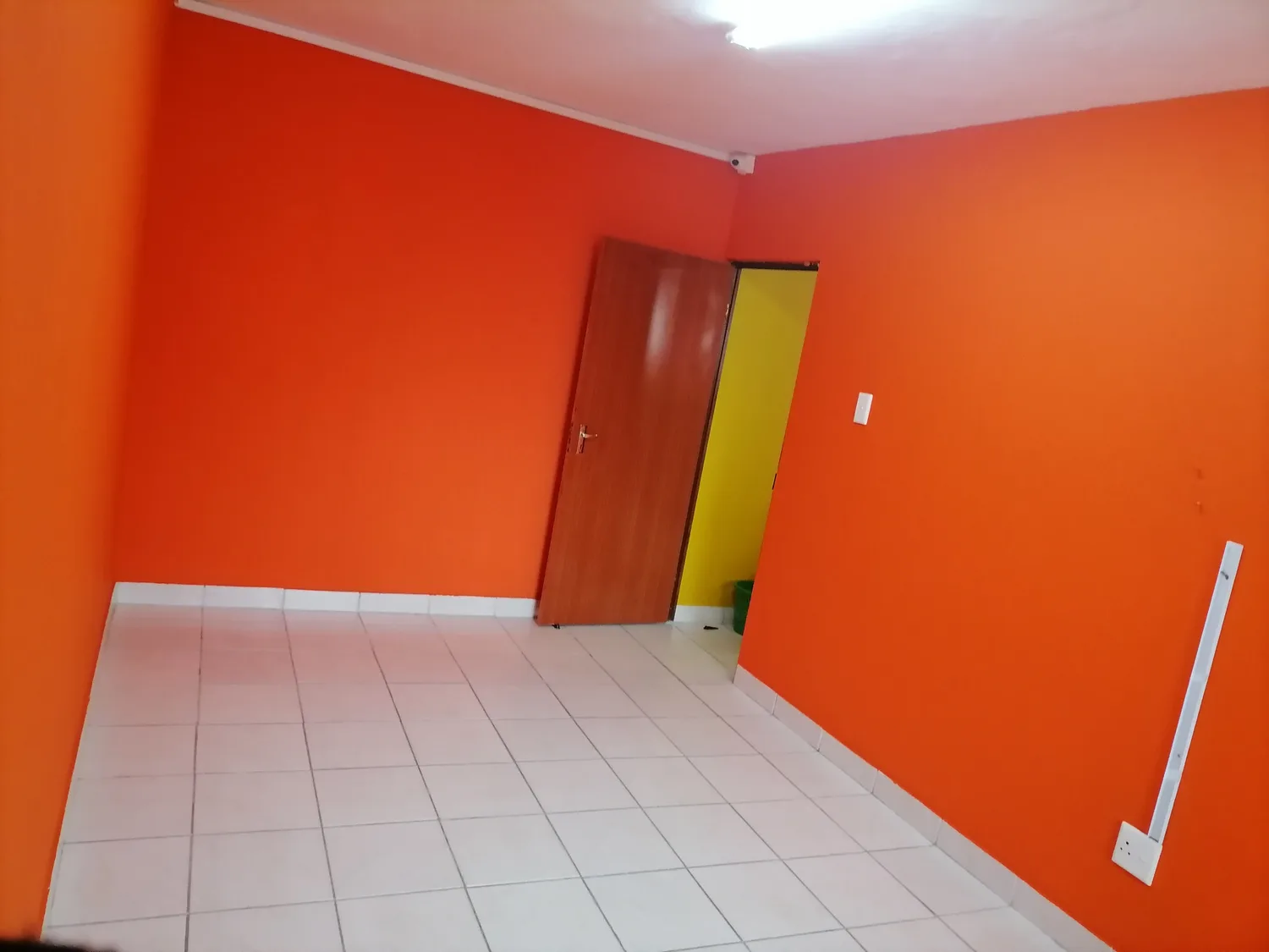 A bright orange-painted playroom with white tiled floors and a wooden door.