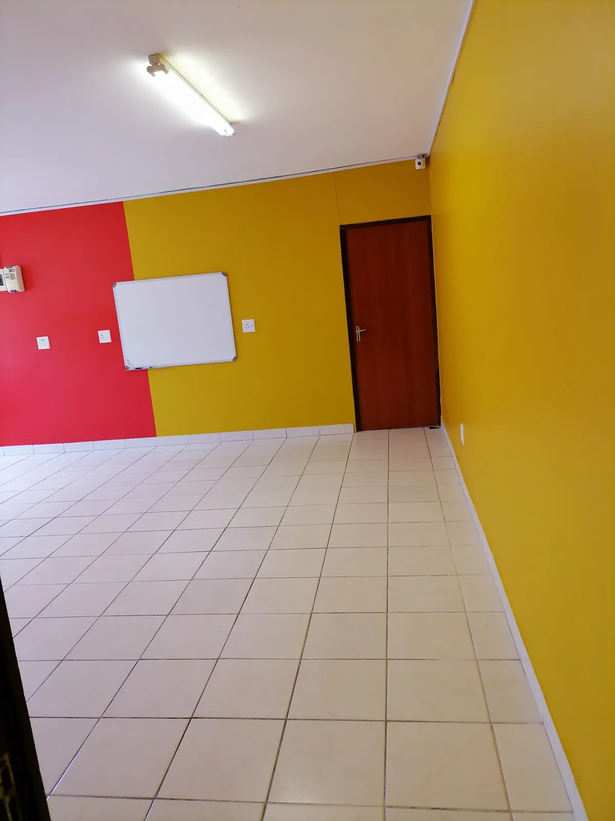 A bright classroom with yellow and red walls, a whiteboard and white tiled floors.