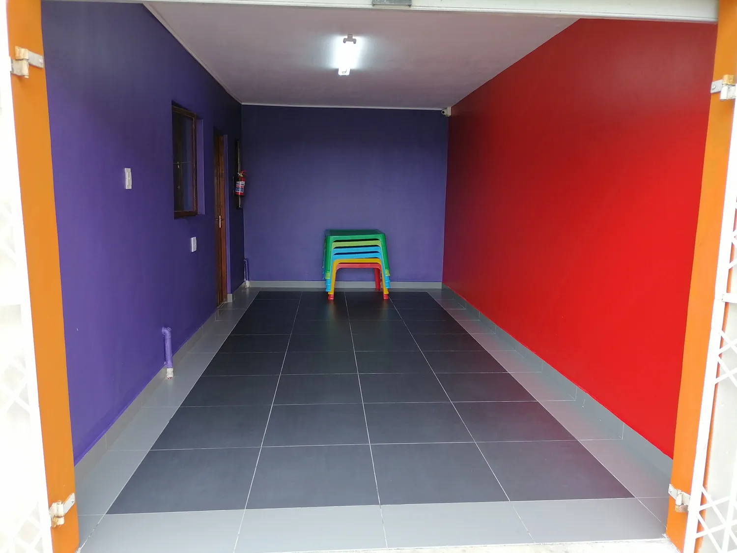 A purple and red classroom with a stack of small colourful chairs waiting on the tiled floor.