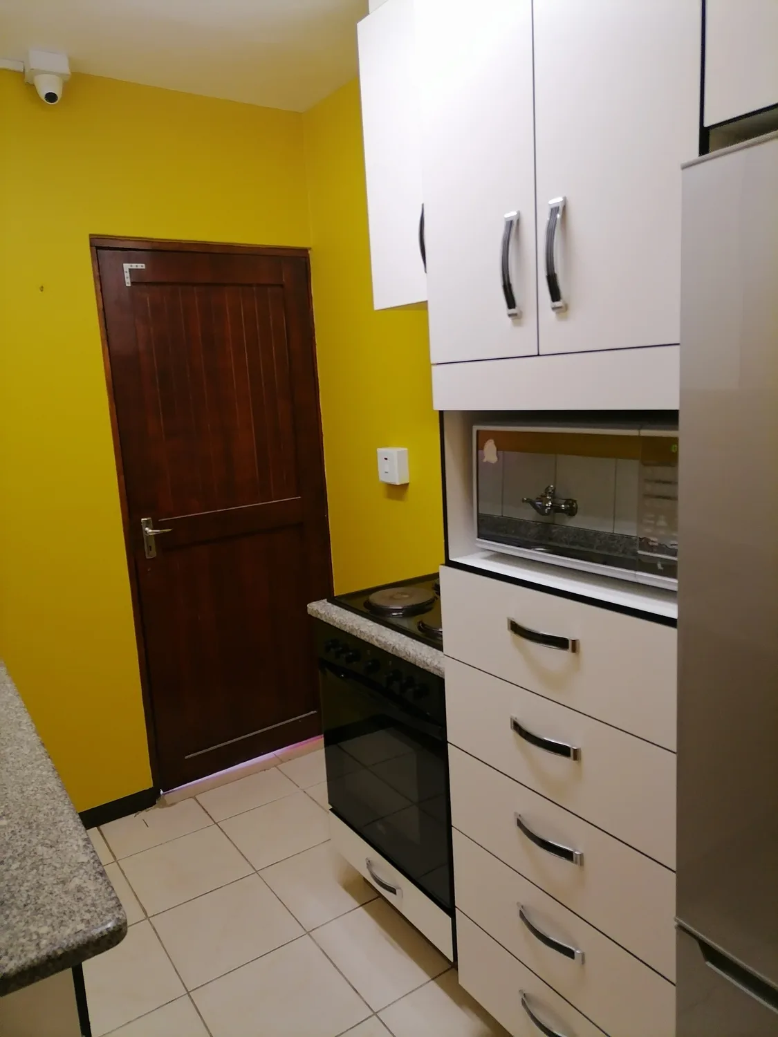 The school kitchen with white cupboards, a stove, microwave and fridge, painted bright yellow.
