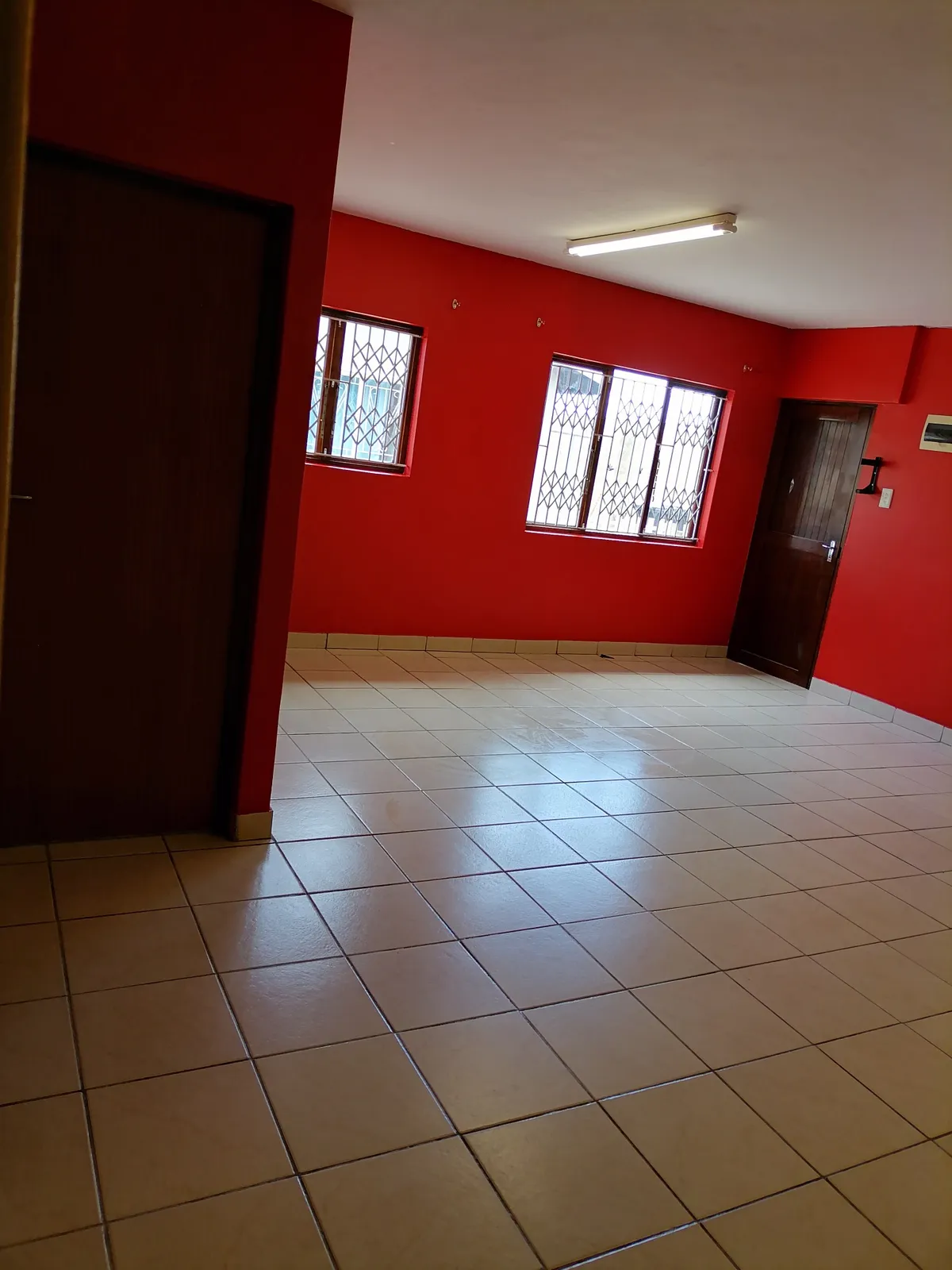 A large red-painted room with barred windows, tiled floors and wooden doors.