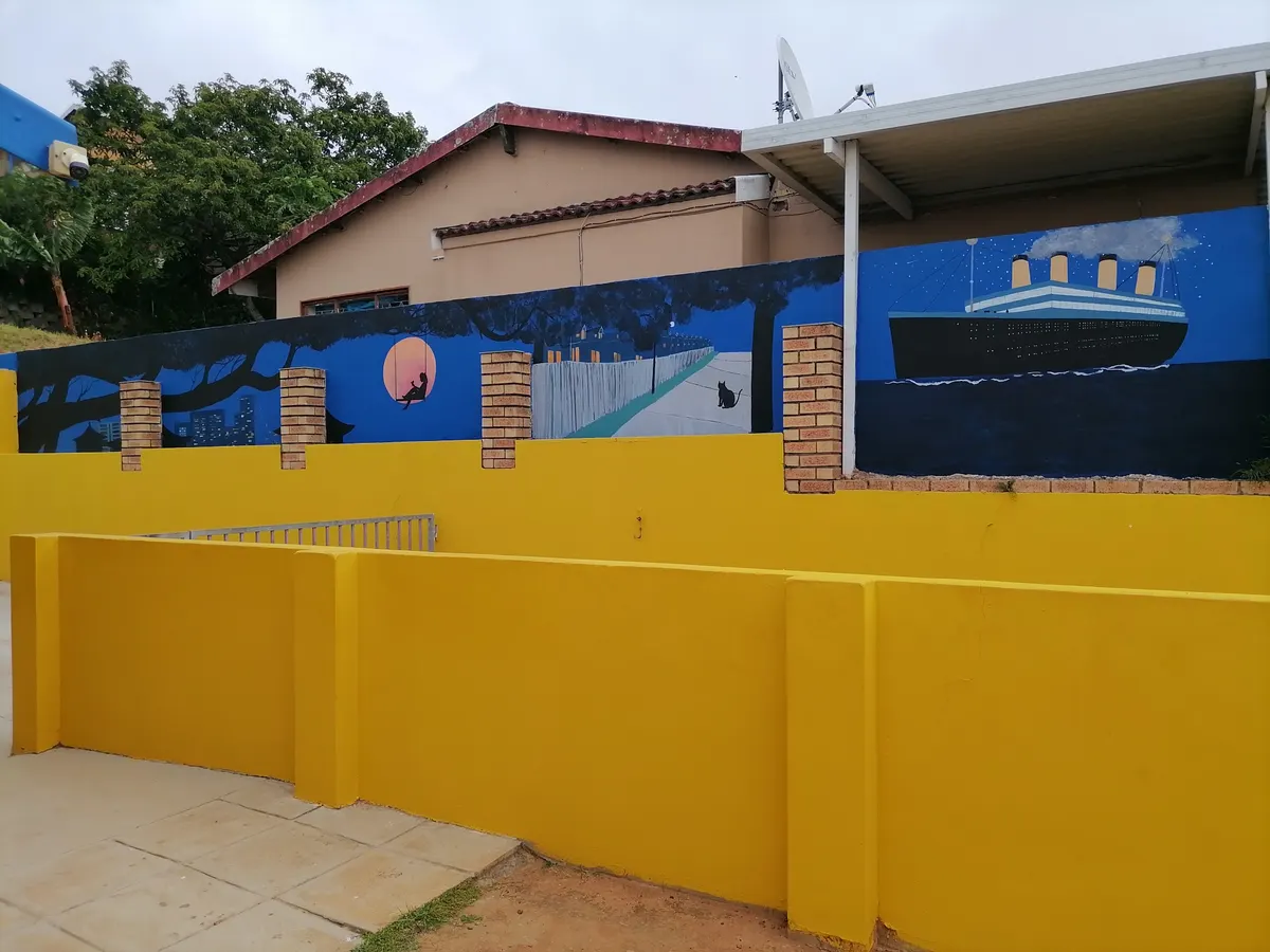 A mural on the school's yellow garden wall showing a night-time city scene and a large ocean liner.